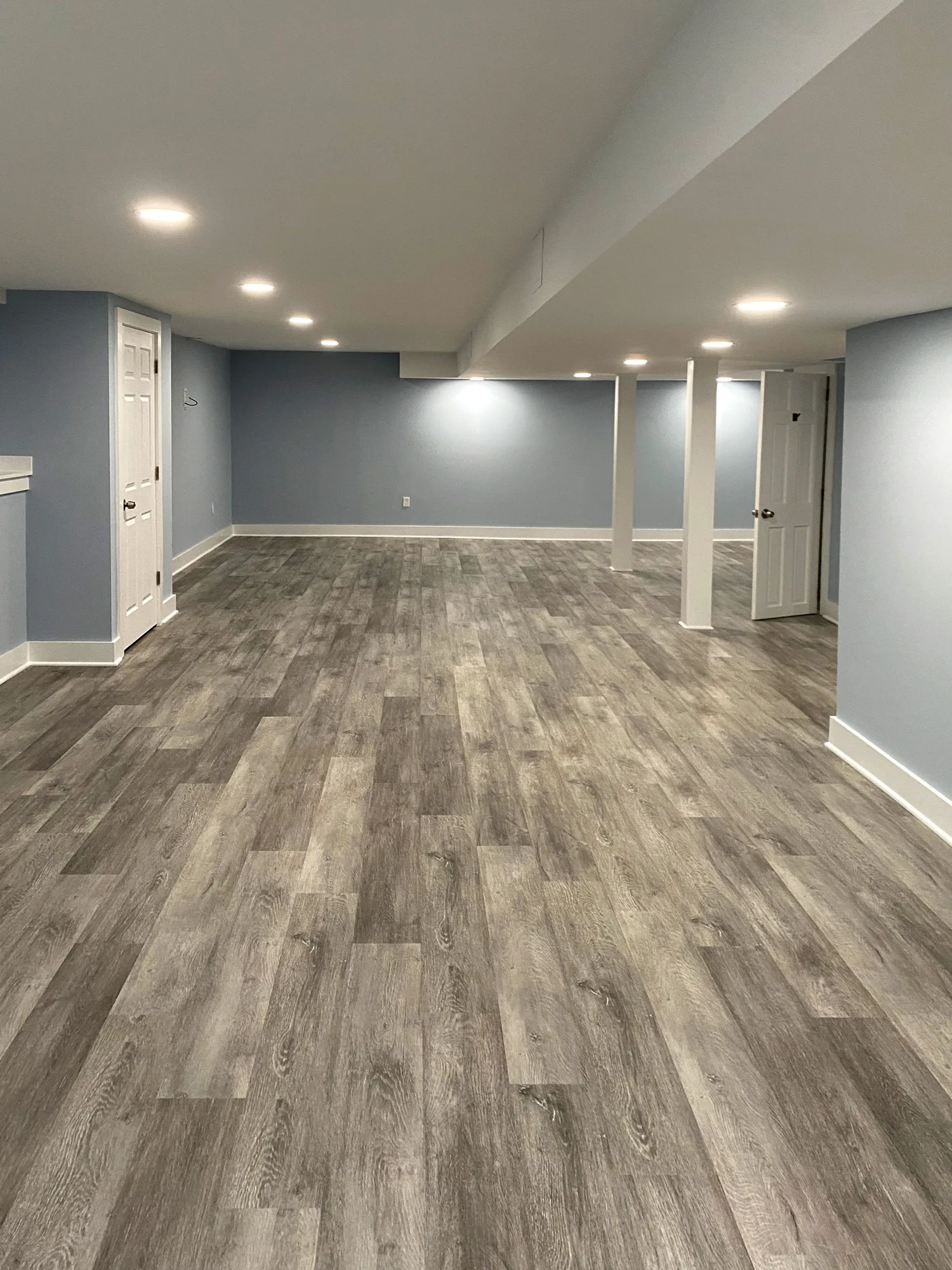 Basement vinyl plank flooring installation showing open layout and support columns